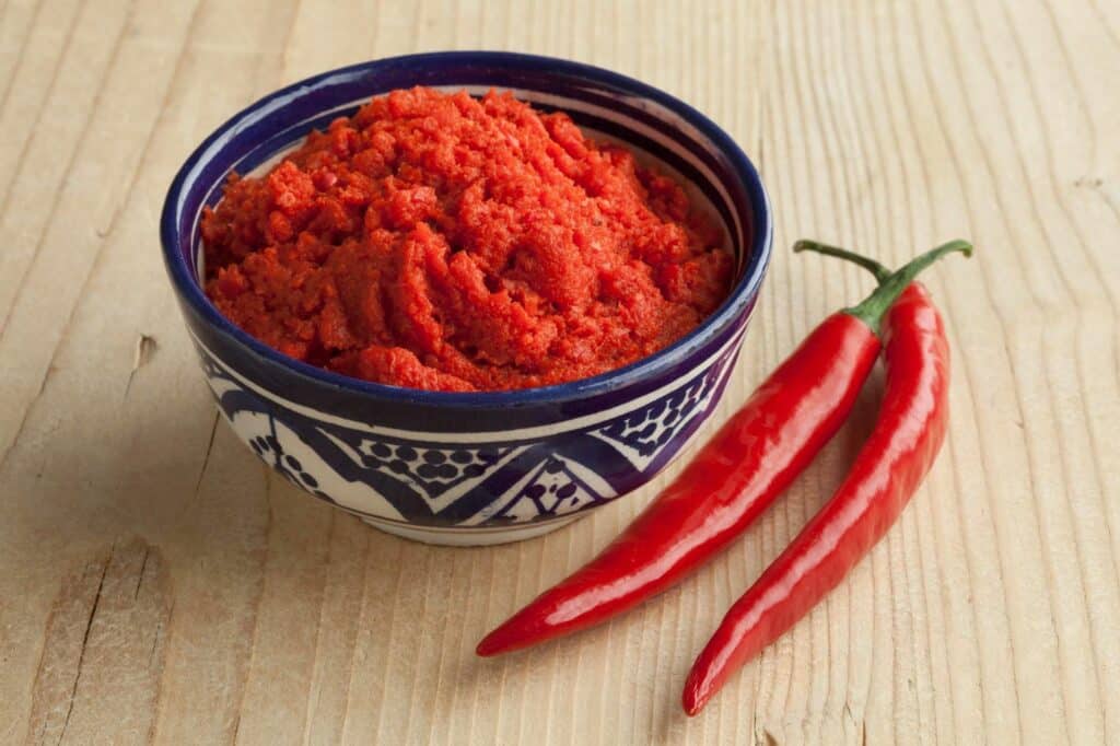 Bol d’harissa avec deux piments rouges posés à côté.